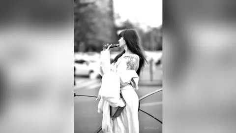 Stylish woman in a white coat drinking coffee on a city street in a moody black and white portrait.