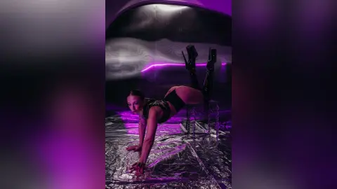 Athletic woman in black bodysuit posing on a silver foil floor in a moody purple lit studio.