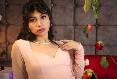 Elegant woman in a pale pink dress posing gracefully against a tufted grey backdrop with red roses.