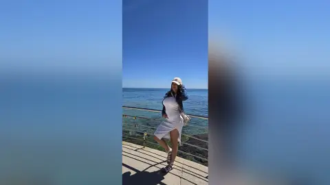 Pregnant woman in a white summer dress and cap relaxing by the ocean on a sunny day.