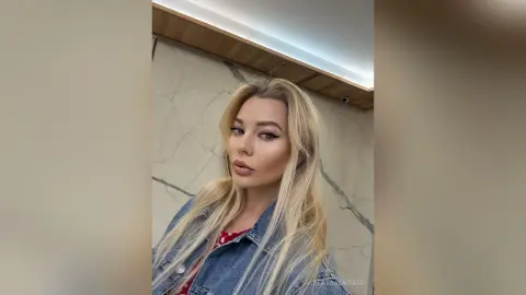 Blonde woman in a denim jacket posing with a confident expression in a modern marble interior.