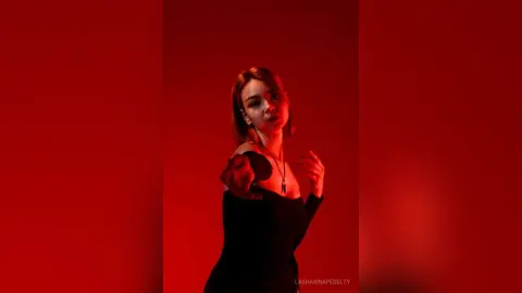 Moody portrait of a woman in a black dress against a dramatic red background.