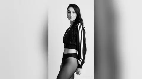Elegant woman in a black Adidas tracksuit posing against a white background in a moody black and white portrait.
