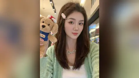 Young woman in a mint green cardigan holding a teddy bear in a bright indoor setting.