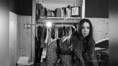 Black and white portrait of a woman in a patterned bodysuit posing in a bedroom with an open closet.