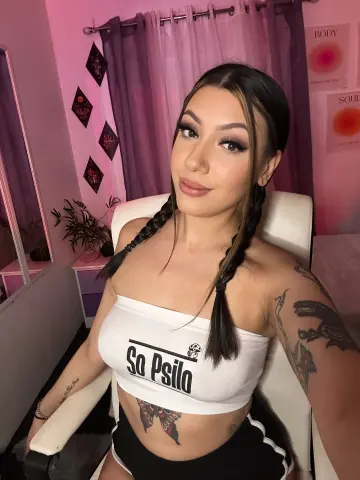 Young woman with long braids in a white crop top sitting in a room with pink lighting and moody vibes.