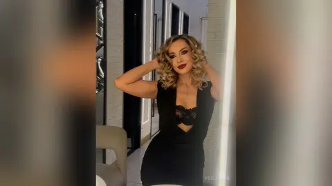 Glamorous woman in a black lace cutout dress posing confidently in a modern bright room.