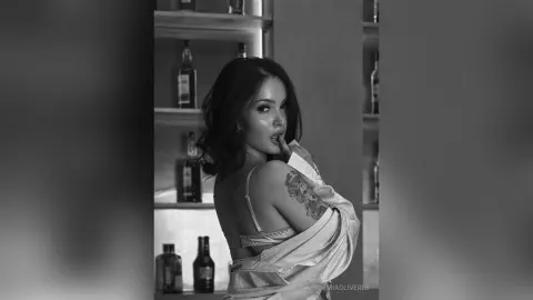 Glamorous woman in a satin robe posing thoughtfully in a moody, dimly lit bar setting.