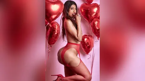 KiaraParker poses in red fishnet lingerie and red heels against a background of red heart-shaped balloons.