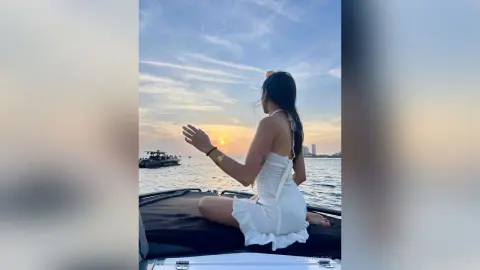 Woman in a white summer dress sitting on a boat at sunset overlooking the ocean.
