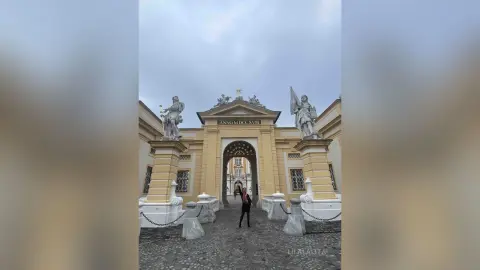 Woman in a black outfit standing before a grand historic white and yellow classical building under a cloudy sky.