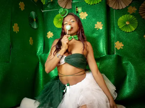 Woman in green and white festive outfit eating a lollipop against a sparkly green St. Patrick's Day backdrop.