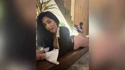 Young woman with long dark hair in a black and white outfit lounging playfully on a wooden bench indoors.