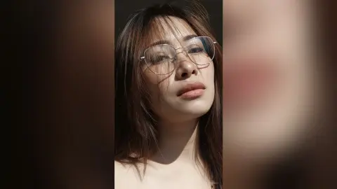 Close-up portrait of a woman with glasses in warm sunlight creating a soft, cinematic mood.