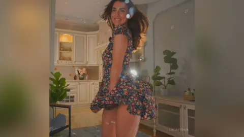 Smiling woman in a floral print mini dress posing in a bright, modern living room.