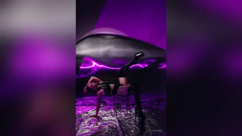 Edgy woman in black leather outfit posing in a moody, neon purple lit studio setting.