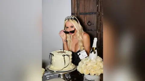 Blonde woman in black outfit celebrating with cake and champagne in a festive mood.
