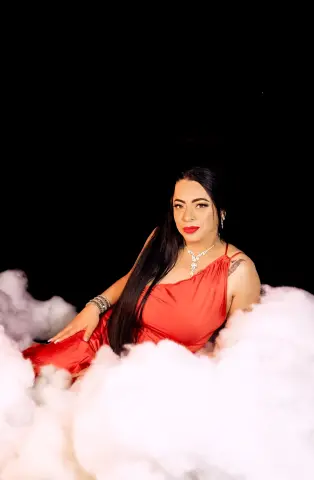 Elegant woman in a red silk dress sitting amidst soft white clouds against a dark background.