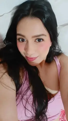 Smiling young woman with long black hair wearing a pink ribbed tank top in a bright indoor setting.