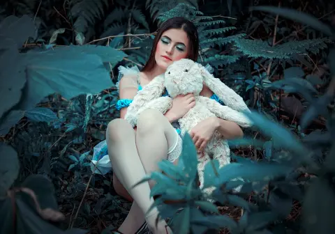 AlicceGray holds a large white stuffed bunny while sitting in thick green leaves and ferns.