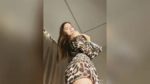 Young woman in a stylish leopard print dress posing confidently in a bright, minimalist indoor setting.