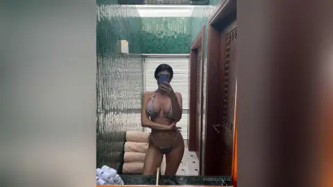 Woman in a patterned bikini taking a mirror selfie in a modern green tiled bathroom.