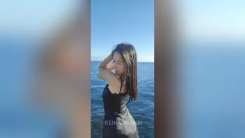 Young woman in a black dress enjoying a peaceful summer day by the blue ocean.