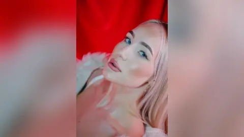 MarryDavies poses close-up against a red background, showing her blonde hair and light blue eyes.