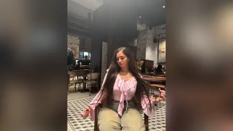 Young woman in a pink ruffled blouse sitting in a moody, modern cafe with tiled floors.