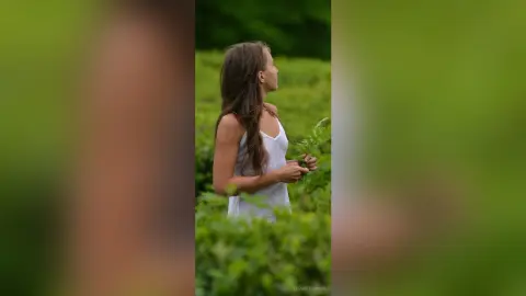 Dreamy portrait of a young woman in a white summer dress holding ferns in a lush green meadow.