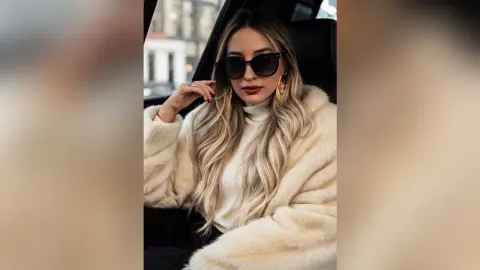 Stylish blonde woman in a white fuzzy coat and sunglasses sitting in a car with a chic winter fashion mood.