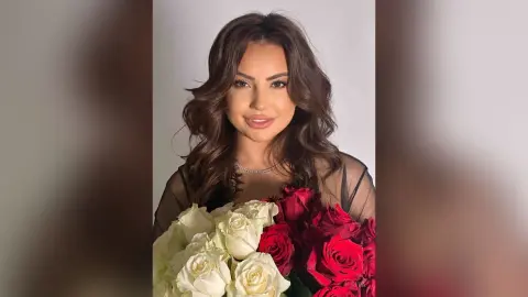 Elegant woman in a black dress holding a large bouquet of red and white roses in a studio setting.