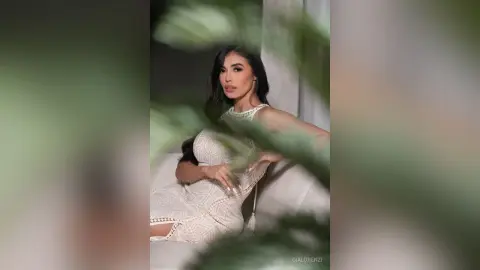 Elegant woman in a white lace cocktail dress sitting on a sofa in a soft, moody indoor setting.
