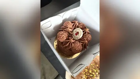 Delicious chocolate mousse cake topped with chocolate truffles in a white bakery gift box.
