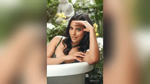 Smiling woman in a green lace dress relaxing in a lush garden setting with white flowers.