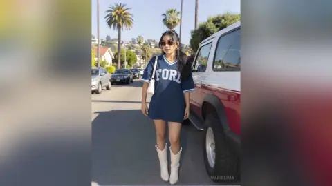 Stylish woman in navy oversized graphic t-shirt and white boots standing by a red SUV on a sunny street.