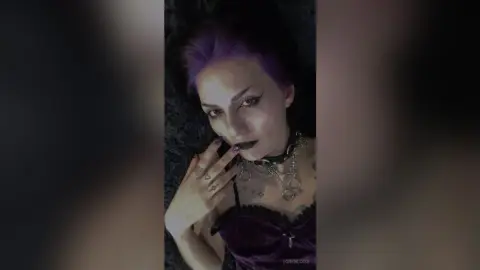 Moody portrait of a woman with purple hair wearing a black lace corset and silver necklaces.