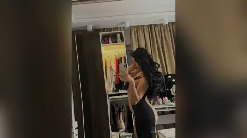NicoleBella poses in a black bodysuit while taking a mirror selfie in her bedroom.
