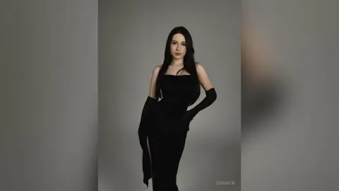 Elegant woman in a sleek black evening gown and long gloves posing against a minimalist grey studio background.