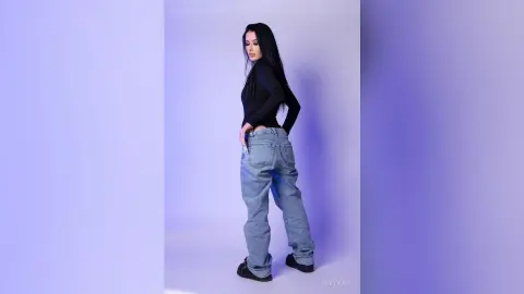Young woman in a black long-sleeve top and baggy blue jeans posing against a minimalist lavender studio background.