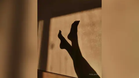 Silhouette of bare feet against a sunlit wall in a warm, minimalist indoor setting.