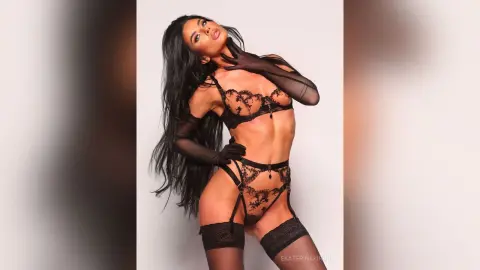 Fit woman with long dark hair wearing black lace lingerie and sheer gloves in a studio setting.