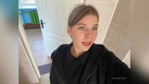 Young woman with brown hair wearing a black hoodie in a bright, modern indoor setting.