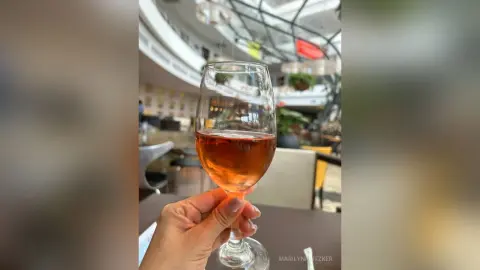 Hand holding a glass of rose wine in a bright, modern restaurant setting during a relaxing afternoon.