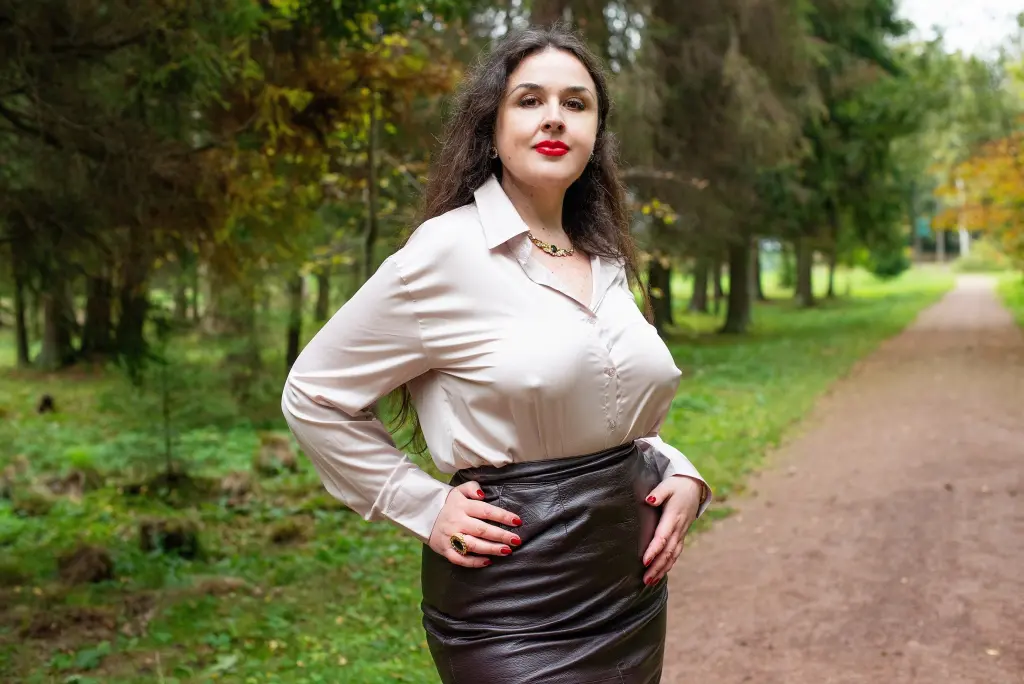 StepMomNextDoor poses with her long dark hair while wearing a black mesh-top bodysuit against a white background.