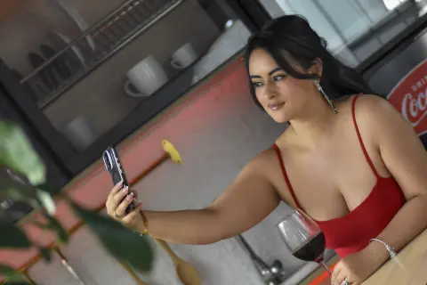 Smiling woman in a red tank top taking a selfie in a modern kitchen setting.