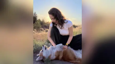 Young woman in a white t-shirt petting a happy corgi dog in a sunny outdoor field at sunset.