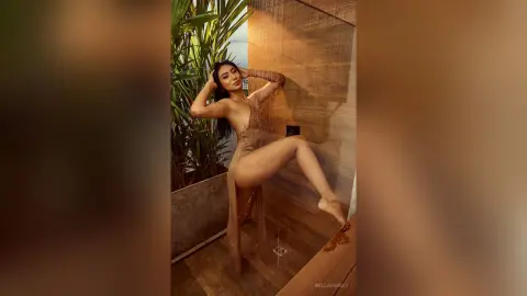 Glamorous woman in a sheer nude dress posing elegantly in a modern luxury shower setting.