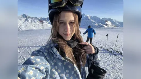 Smiling woman in floral ski jacket and helmet enjoying a sunny day on a snowy mountain resort.