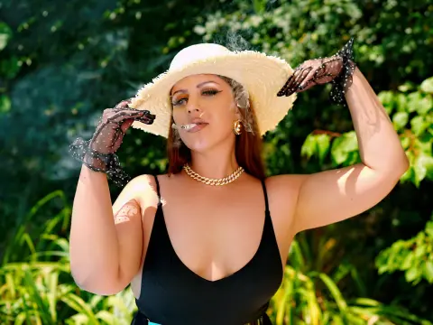 Glamorous woman in a black swimsuit and straw hat posing outdoors in a lush green garden.